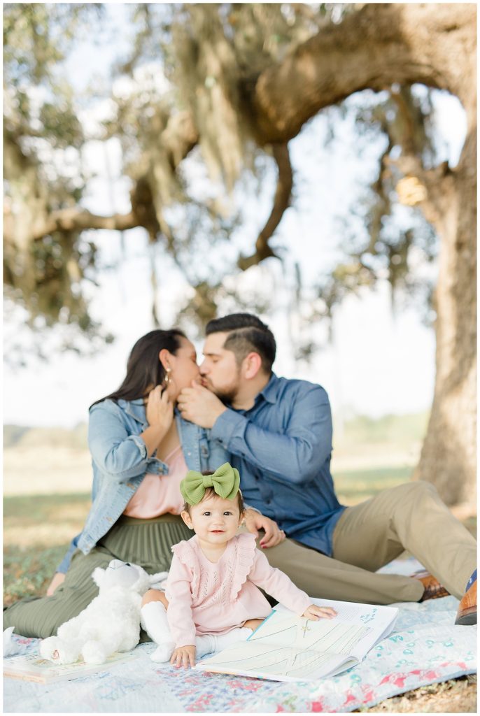 Baby smiling at the camera while mom and dad kiss in the background for a 2019 Holiday Mini Session in San Antonio, TX with Award Winning San Antonio Family Photographer Monica Roberts Photography | www.monicaroberts.com