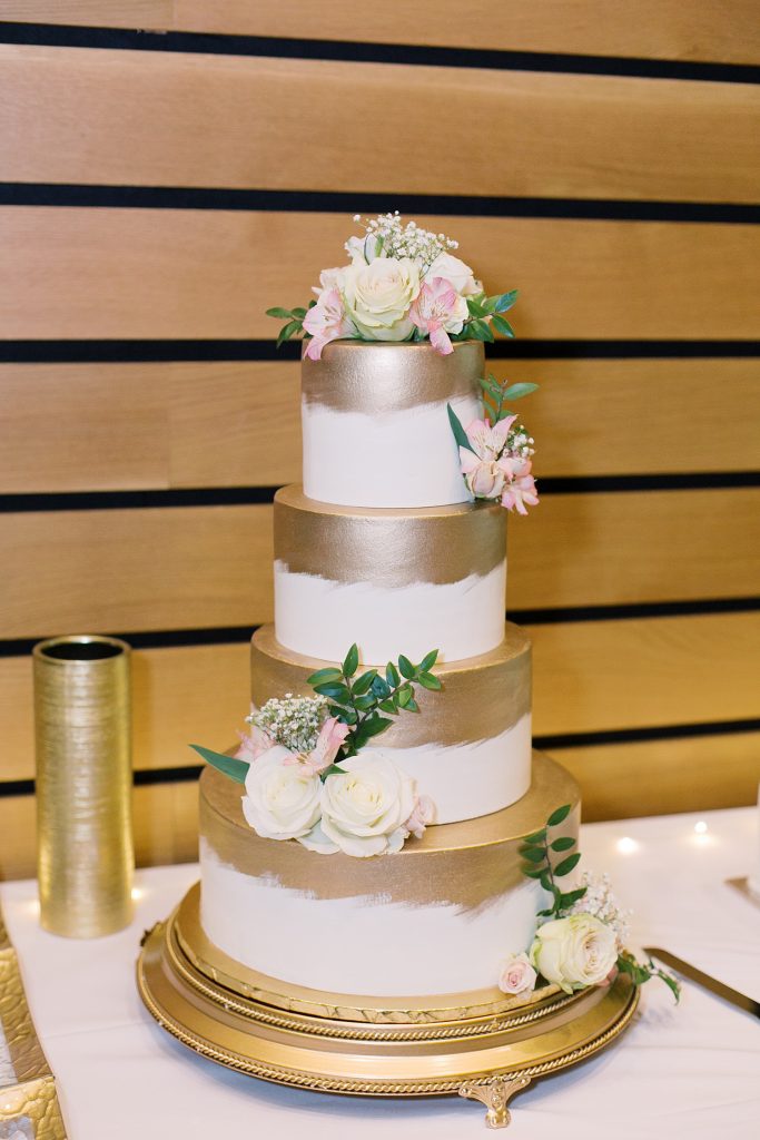 4 tier gold and white wedding cake with pink flowers for a wedding at the Jack Guenther Pavilion at the Briscoe in San Antonio with Monica Roberts Photography - https://monicaroberts.com/