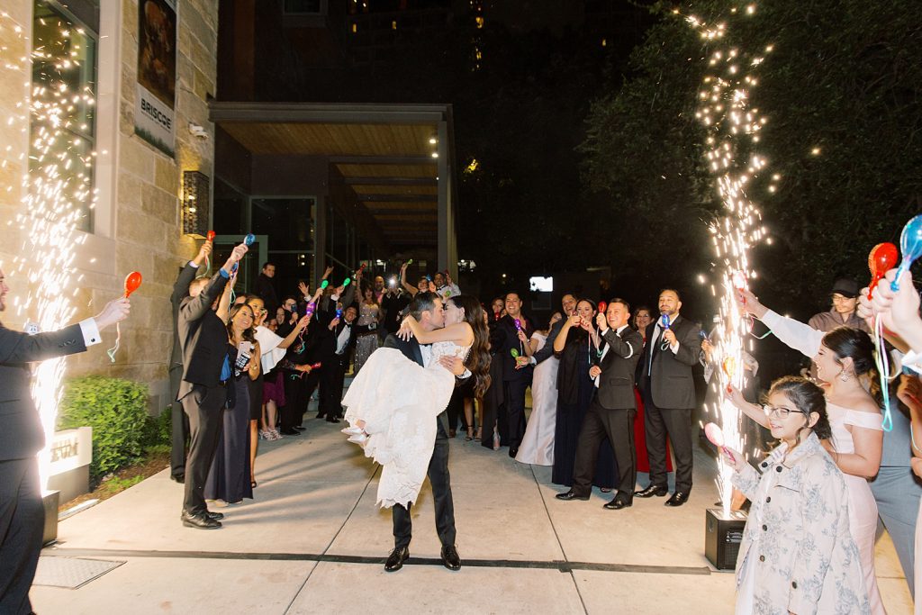 groom picks up his bride for their grand exit with water sparklers for a wedding at the Jack Guenther Pavilion at the Briscoe in San Antonio with Monica Roberts Photography - https://monicaroberts.com/