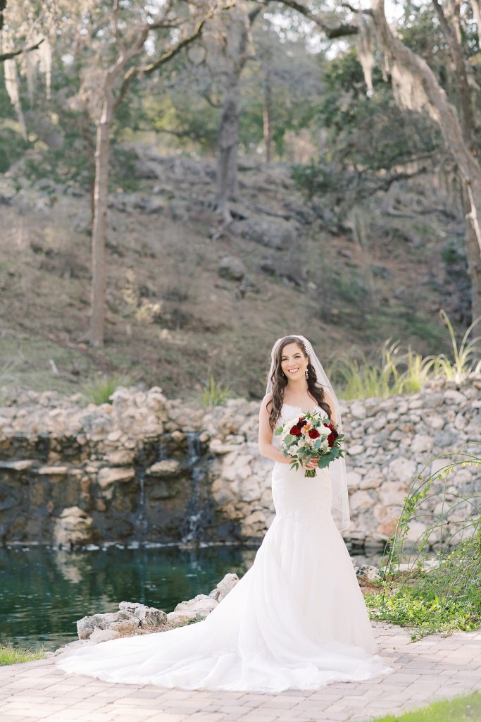 bride in wedding dress standing in front of a waterfall under moss trees for her Bridal Portraits at Hayes Hollow in Spring Branch, TX with Monica Roberts Photography www.monicaroberts.com