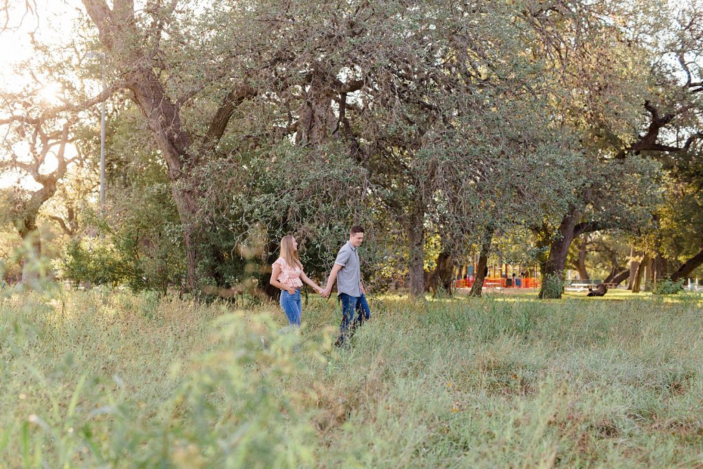 couple walking holding hands in a field in Downtown San Antonio for their engagement session with Monica Roberts Photography https://monicaroberts.com